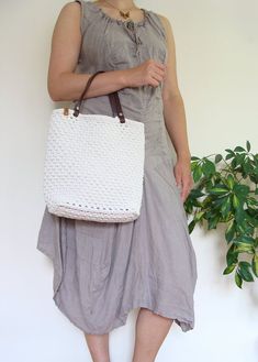 a woman holding a white purse standing next to a plant