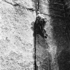 a man climbing up the side of a rock with a rope attached to his back