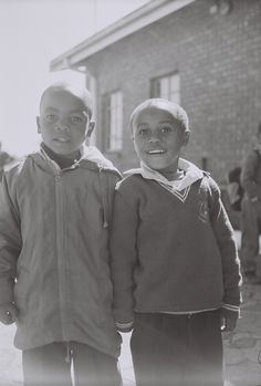 two young boys standing next to each other in front of a brick wall and building