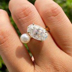 a woman's hand holding a ring with a diamond and a pearl on it