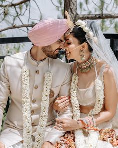 a man and woman sitting next to each other on a bench wearing white outfits with flowers in their hair