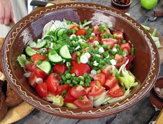 a large bowl filled with lots of veggies on top of a wooden table