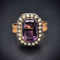 "Amethyst stones have been thought for generations to provide protection and were worn by the Ancients as a talisman for luck. The beautiful violet purple hue has also had an allure not to be resisted. Beloved by Victorians as well, it was the first color a widow was allowed to wear after coming out of mourning.  This ring was converted from an antique brooch. The beautiful, faceted rectangular amethyst is haloed by 21 natural seed pearls, which the Victorian jewelers implemented to represent \"tears of sorrow\". The faceted emerald cut amethyst stone is paired with a replica textured band, giving its new incarnation as a ring is a lovely way to showcase this classic combination of amethyst and pearl.   Details (approximate) Size: 7 Weight:  5 grams Materials: Gold, Amethyst, Seed Pearl Me Fine Jewelry Purple Amethyst Multi-stone Ring, Purple Multi-stone Amethyst Ring Fine Jewelry, Purple Multi-stone Amethyst Ring In Fine Jewelry Style, Purple Multi-stone Amethyst Ring, Antique Purple Amethyst Ring With Accent Stones, Purple Amethyst Gemstone With Center Stone, Oval Purple Amethyst Ring With 17 Jewels, Amethyst Ring With 17 Jewels For Anniversary, Heirloom Purple Amethyst Ring With Center Stone