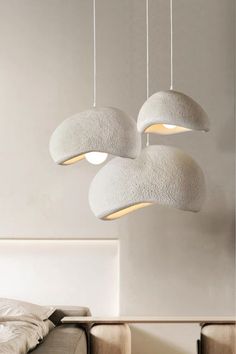 three lights hanging from the ceiling above a bed in a room with white walls and furniture