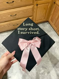 a graduation cap that says long story short, i survived with pink ribbon on it