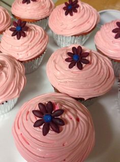 cupcakes with pink frosting and purple flowers on them sitting on a plate