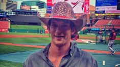 a man wearing a cowboy hat standing in front of a baseball field at a stadium