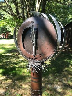 a metal sculpture sitting on top of a wooden pole in the middle of a park