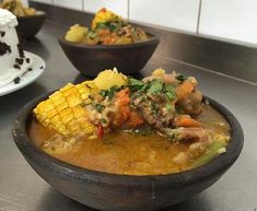 a bowl of soup with corn on the cob and other dishes in the background