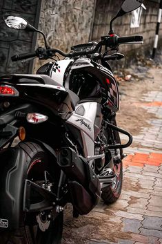 a black and silver motorcycle parked in front of a building on a brick sidewalk next to a wall