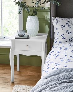 a bedroom with a bed, nightstand and plant on the table in front of the window