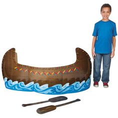 a boy standing next to a cardboard boat and paddles