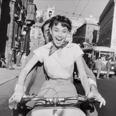 a woman riding on the back of a scooter down a street