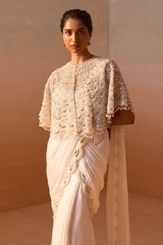 White poncho sleeves cape with all over scallop embroidery using silver nalki zircon and pearl highlights. Paired with a scallop embroidered border pre-draped saree with ruffled hem and a bustier. - Aza Fashions Cutdana Cape Sleeve Wedding Dress, Elegant Dresses With Cutdana And Cape Sleeves, Reception Blouse With Cutdana And Traditional Drape, Traditional Drape Blouse With Cutdana For Reception, Bollywood-style Draped Wedding Blouse Piece, Festive Embellished Pre-draped Saree, Wedding Unstitched Blouse Piece With Cape Sleeves, Draped Blouse With Zari Work For Wedding, Wedding Blouse With Resham Embroidery And Draped Shape