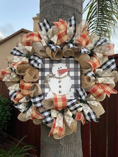 a wreath with a snowman on it hanging from a tree in front of a house