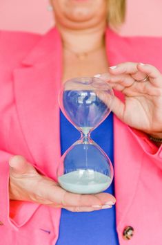 a woman in pink jacket holding an hourglass with blue liquid inside and sand running through it