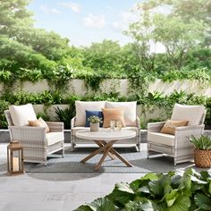 an outdoor patio with white wicker furniture and green plants on the wall behind it