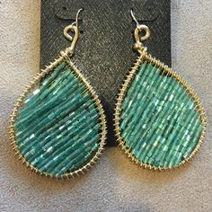 a pair of green and gold earrings sitting on top of a black piece of cloth