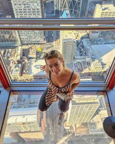 a woman standing on the edge of a glass floor in a high rise building looking at the camera