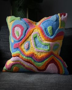 a multicolored pillow sitting on top of a couch next to a potted plant