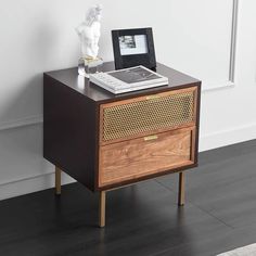 a nightstand with a book on top of it next to a white vase and statue