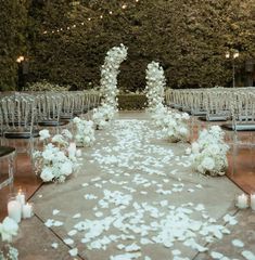 an outdoor wedding ceremony with white flowers and candles on the aisle, surrounded by clear chairs