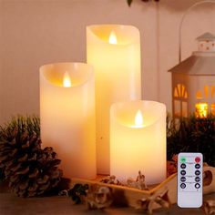 three lit candles sitting on top of a table next to a remote control and pine cones