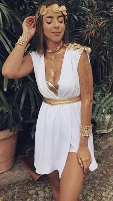 a woman in a white dress and gold jewelry standing next to a potted plant