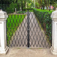 an iron gate in the middle of a sidewalk with two white pillars and one black fence