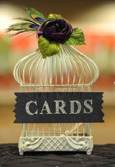 a birdcage with a purple flower on top of it and the words cards in front of it