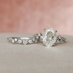 two engagement rings with diamonds on them sitting on a table next to a pink background