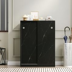 a black cabinet sitting on top of a wooden floor next to a white basket and umbrella