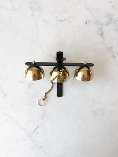 two brass bells hanging from a black hook on a white marble wall with gold accents