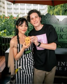 a man and woman standing next to each other in front of a sign holding food