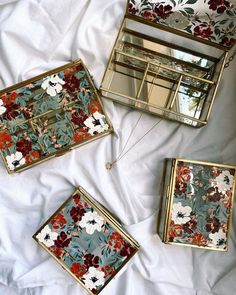 three decorative mirrors sitting on top of a white bed covered in sheets and pillows with floral designs