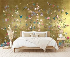 a bed sitting in front of a green wall with flowers on it and birds flying around