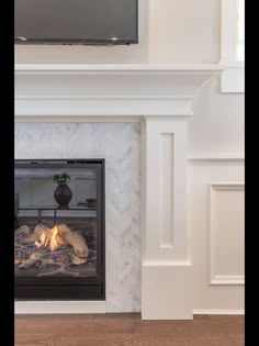 a fireplace with a television above it in a room that has white walls and wood floors