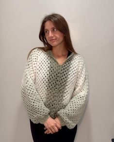 a woman standing in front of a wall wearing a white sweater and black leggings