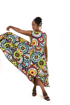 A woman posing in a bright multi-colored African print high-low maxi dress. Asymmetrical Multicolor Maxi Dress, Bohemian Multicolor A-line Sleeveless Dress, Asymmetrical Multicolor Maxi Dress For Beach, Flowy Multicolor Floral Print Sleeveless Dress, Multicolor Print Sleeveless Midi Sundress, Sleeveless Multicolor Sundress Midi Dress, Summer Sleeveless Maxi Dress With Bold Print, Sleeveless Multicolor Patterned Midi Dress, Multicolor Sleeveless Midi Dress With Colorful Pattern