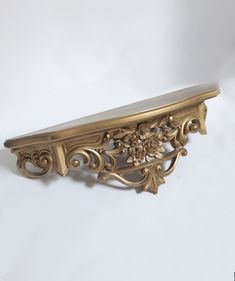 an ornate gold shelf with flowers and leaves on the top, against a white background