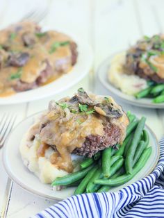 two white plates topped with green beans and mashed potatoes covered in gravy