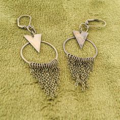 These fun geometric charm earrings come in a subtle antique brass finish. Each earring has a cascade of dainty chains hanging from a hoop in a chainmail reminiscent pattern. These bold and lively earrings are sure to make an impression. With a matching necklace available, this would make a fabulous gift set! -Geometric triangle and hoop charm -hanging chain accents -Antique brass finish -Leverback earring closure Brass Dangling Charms Drop Earrings, Bohemian Triangle Nickel-free Earrings, Geometric Nickel-free Metal Earrings, Nickel-free Geometric Metal Earrings, Nickel-free Geometric Brass Earrings, Vintage Brass Dangle Hoop Earrings, Handmade Triangle Brass Jewelry, Nickel-free Bronze Dangle Hoop Earrings, Handmade Geometric Brass Jewelry