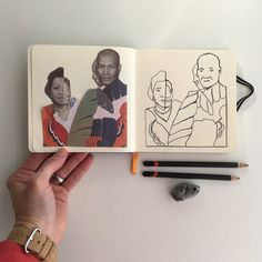 a hand holding an open book with drawings on it and pencils next to it