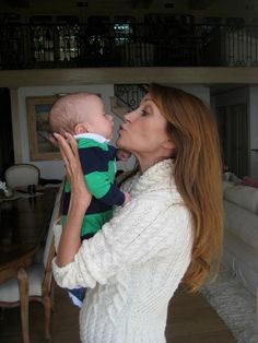 a woman holding a baby in her arms and kissing it's face with both hands