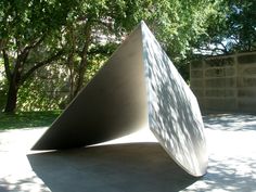 a sculpture in the middle of a park with trees behind it and shadows on the ground