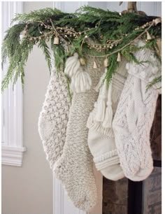 christmas stockings hanging from a mantel decorated with greenery