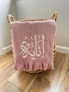 a pink afghan with white arabic writing is sitting on a wooden floor next to a wicker basket