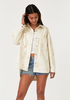 [Color: Natural] A front facing image of a brunette model wearing an off white bohemian shirt jacket crafted from cotton. With long sleeves Spring Relaxed Fit Shacket With Buttoned Pockets, Oversized Embroidered Cotton Outerwear, Casual Outerwear With Floral Embroidery, Bohemian Button-up Summer Outerwear, Spring Cotton Shacket With Buttons, Bohemian Summer Button-up Outerwear, Floral Embroidered Cotton Button-up Outerwear, Embroidered Relaxed Fit Outerwear For Fall, Bohemian Cotton Outerwear With Button Closure