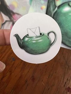 a person holding up a sticker with a teapot on it