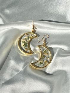 Unique Handmade Pressed Flower Crescent Moon Earrings - Artistic Craftsmanship in Silver Crafted with meticulous attention to detail, this Crescent Moon Earrings set is a true work of art. Here's a glimpse into the process: Flower Selection: Hand-selected flowers are carefully pressed and preserved to capture their natural beauty. Resin Perfection: After drying, the flowers are encased in a slow-cured resin for clarity and durability. Each piece undergoes a meticulous finishing process to addres Whimsical Gold Earrings With Moon Charm, Whimsical Gold Jewelry For Mother's Day, Whimsical Gold Moon Jewelry, Whimsical Moon-shaped Gold Jewelry, Artistic Flower-shaped Jewelry For Crafting, Whimsical Gold Jewelry For Pierced Ears, Whimsical Moon Charm Earrings Gift, Handmade Moon Shaped Artistic Jewelry, Handmade Moon-shaped Artistic Jewelry